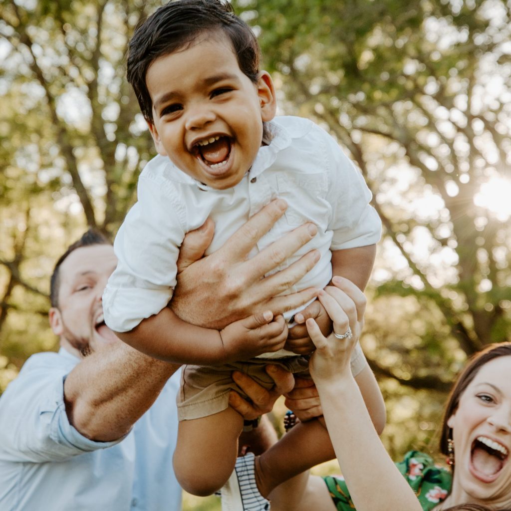 A mom and dad holding their son up towards the camera and all smiling.