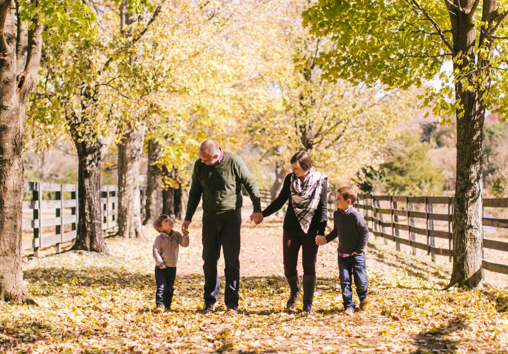 The Magness Family | An image of a mother and father holding hands and walking with their two young boys in a park.