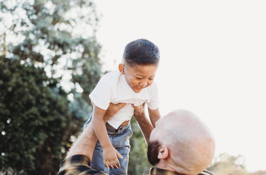 An Image of a young boy being lifted by his father as they laugh in the park