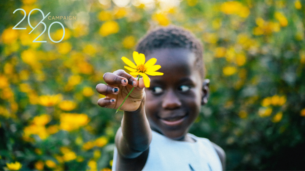 Young girl of a family who received a Show Hope Adoption Aid grant holding a yellow flower up to the camera and smiling.