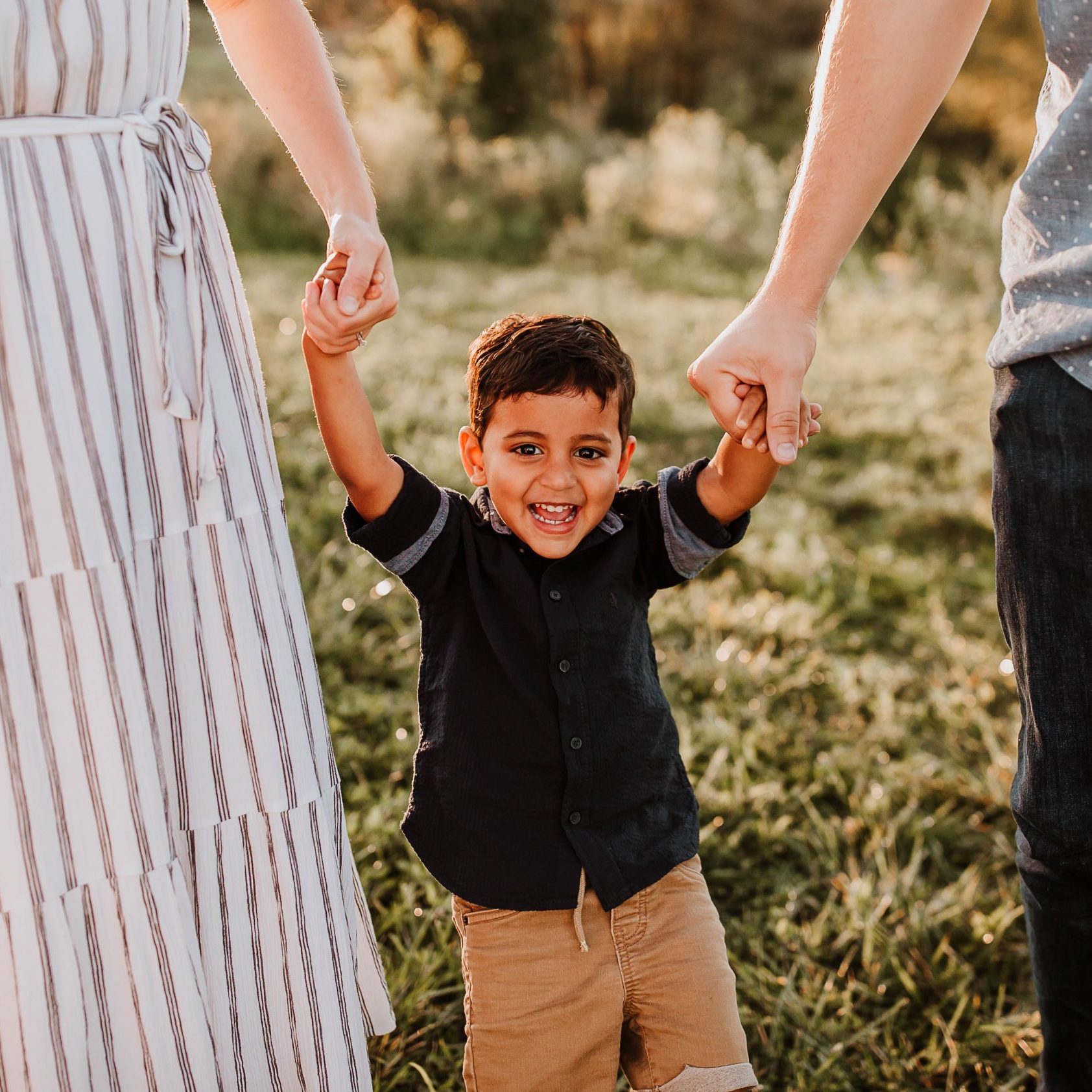 Young boy holding the hands of his mom and dad and smiling